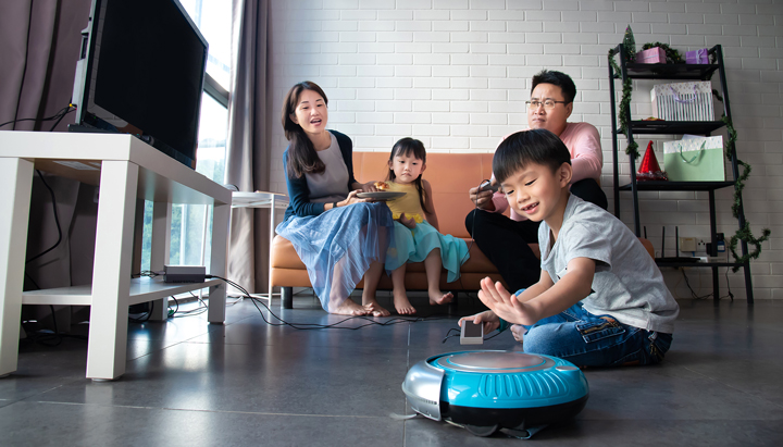 Cheerful family having a leisure moment in their living room and letting the robotic vacuum cleaner do the cleaning, Malaysia, 2019 (photo)