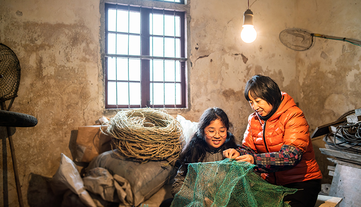 Two women repairing a fishing net under a light. (photo)