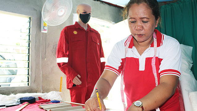 A woman cutting fabric, with a mannikin wearing Shell coveralls in the background, in the Philippines. (photo)