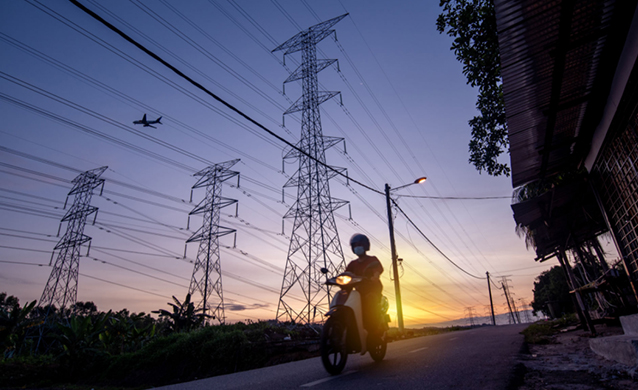 A person riding motorcycle on road in Malaysia at sunset, beside electrical transmission towers with a plane flying overhead. (photo)