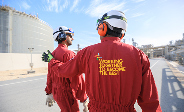 Two worker walking next to a tank. 'Working together to become the best' is written one the back of one of the workers (photo)