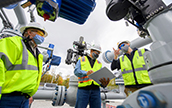 Three men wearing safety equipment and masks discussing safety topics near a pipeline (photo)