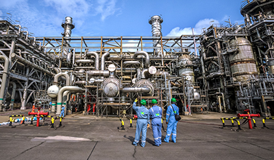 Three men in blue workwear standing in front of the NLNG plant in Bonny, Port Harcourt, Nigeria (photo)