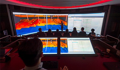 A group of people look at very large screens showing images of the subsurface (photo)