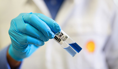 A person with gloves holding two test tubes with a blue liquid inside (photo)