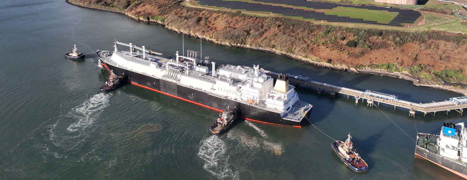 aerial photo of Shell LNG vessel next to pipeline and shoreline with tug boats around (photo)