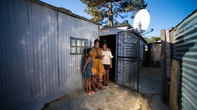 Stellenbosch, Cape Town, South Africa. Standing in front of a corrugated iron home looking at a digital tablet.
(photo)