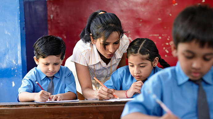 A teacher helps students in blue uniforms with their writing in a classroom (photo)