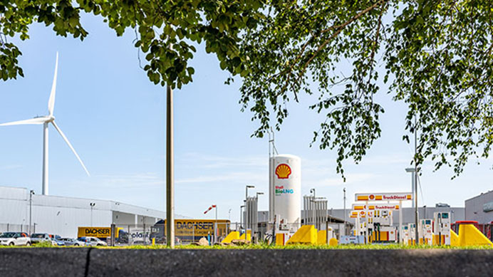 Bio LNG and bio Diesel forecourt next to wind turbine viewed through trees. (photo)
