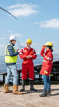 two men and a woman wearing PPE standing together talking next to a solar panel with wind turbine in the background (photo)